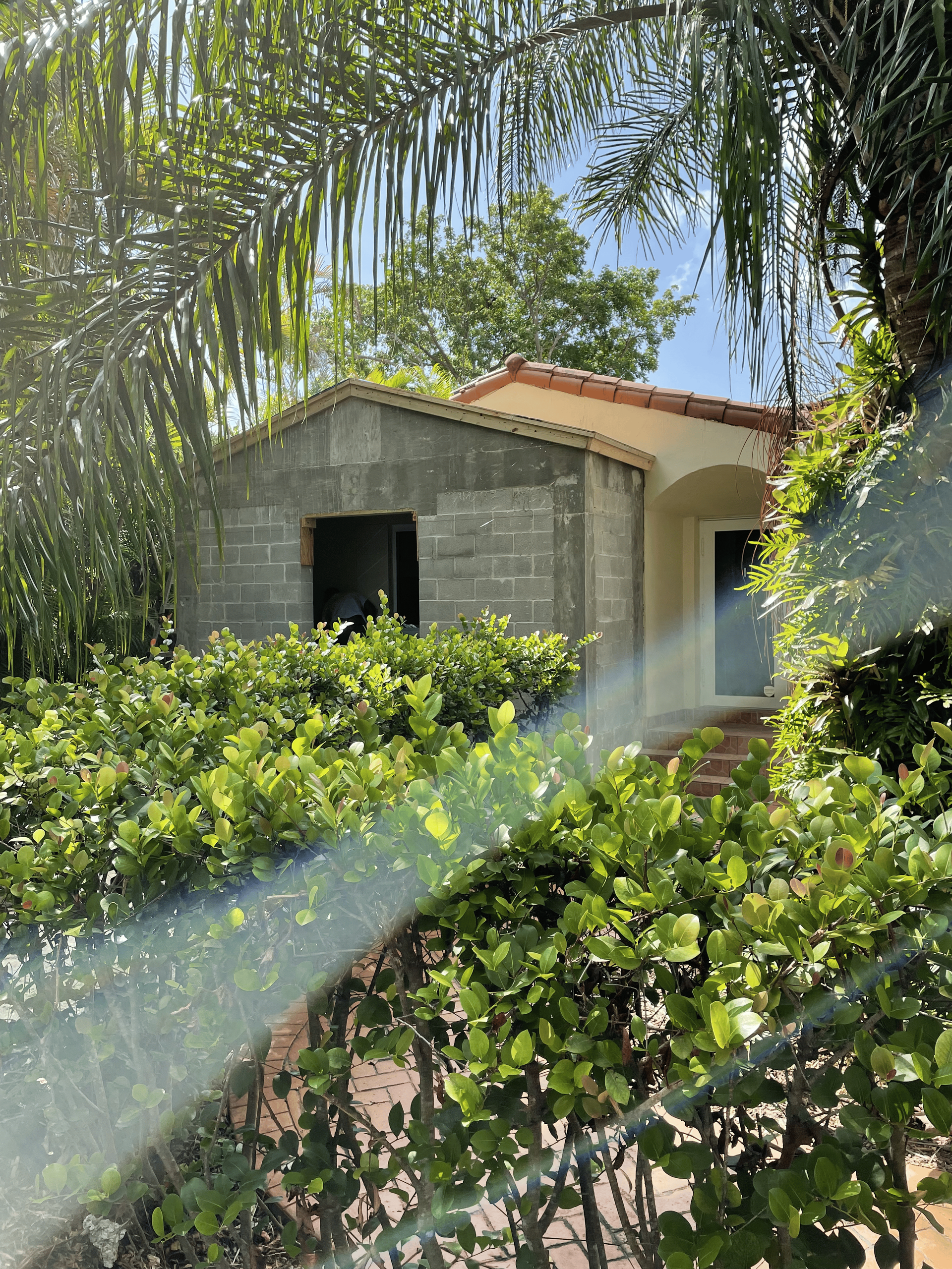Small building with a concrete block side and a stucco side, surrounded by greenery.