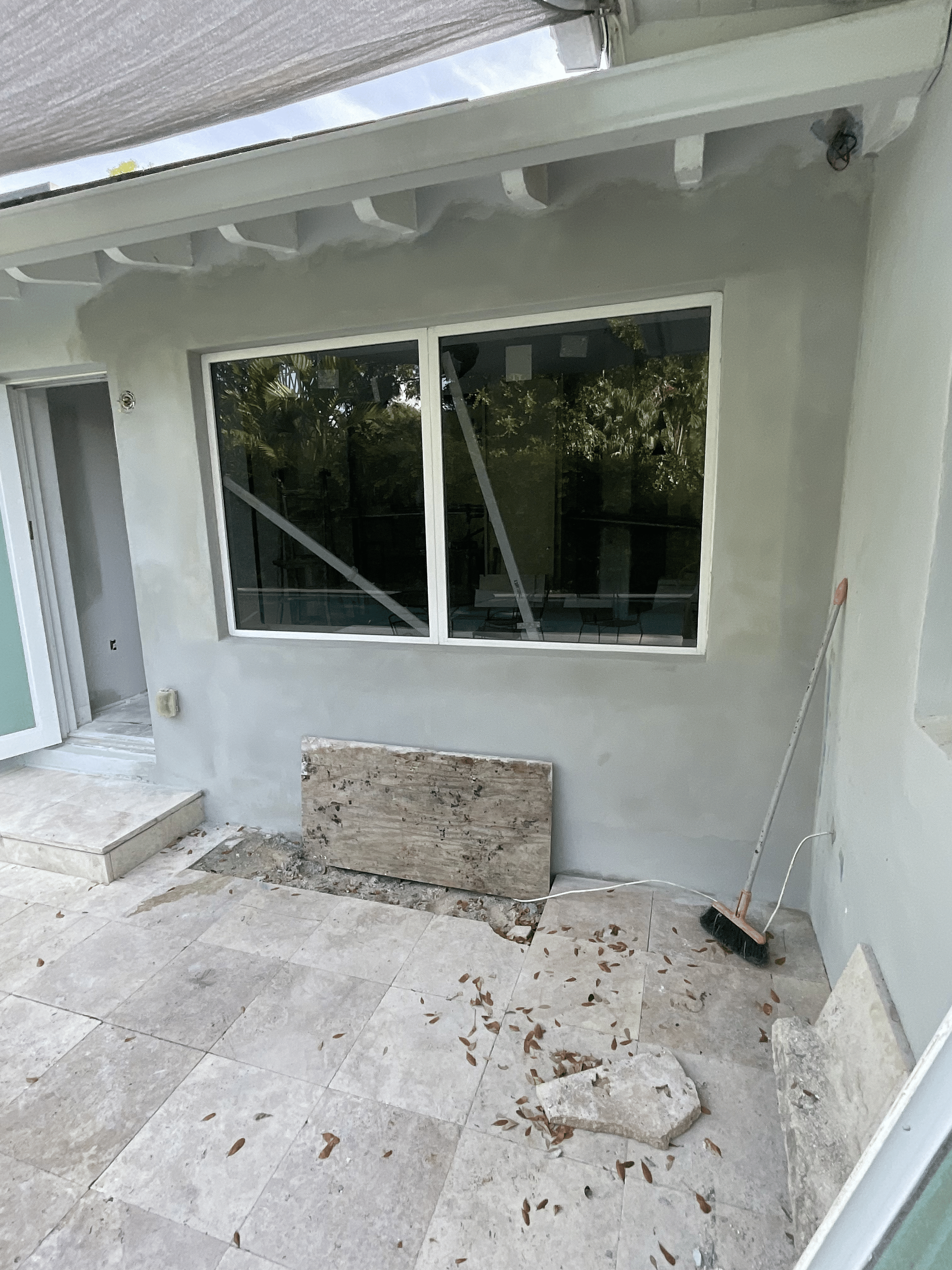 Exterior view of a building with a window and a brush leaning against the wall. The wall is freshly plastered.