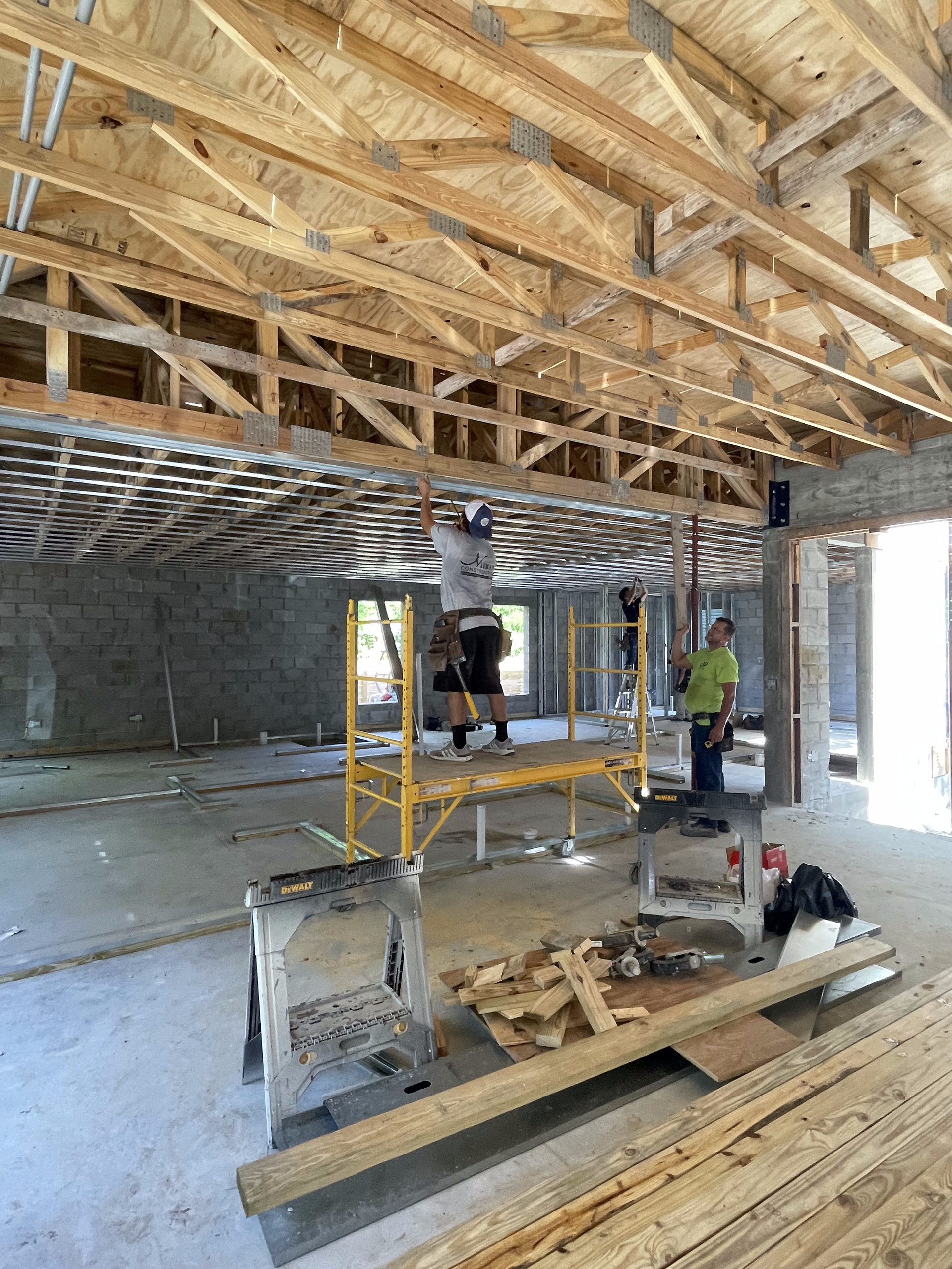 Construction workers on scaffolding, working on a building's interior framing with wood beams and ceiling trusses.