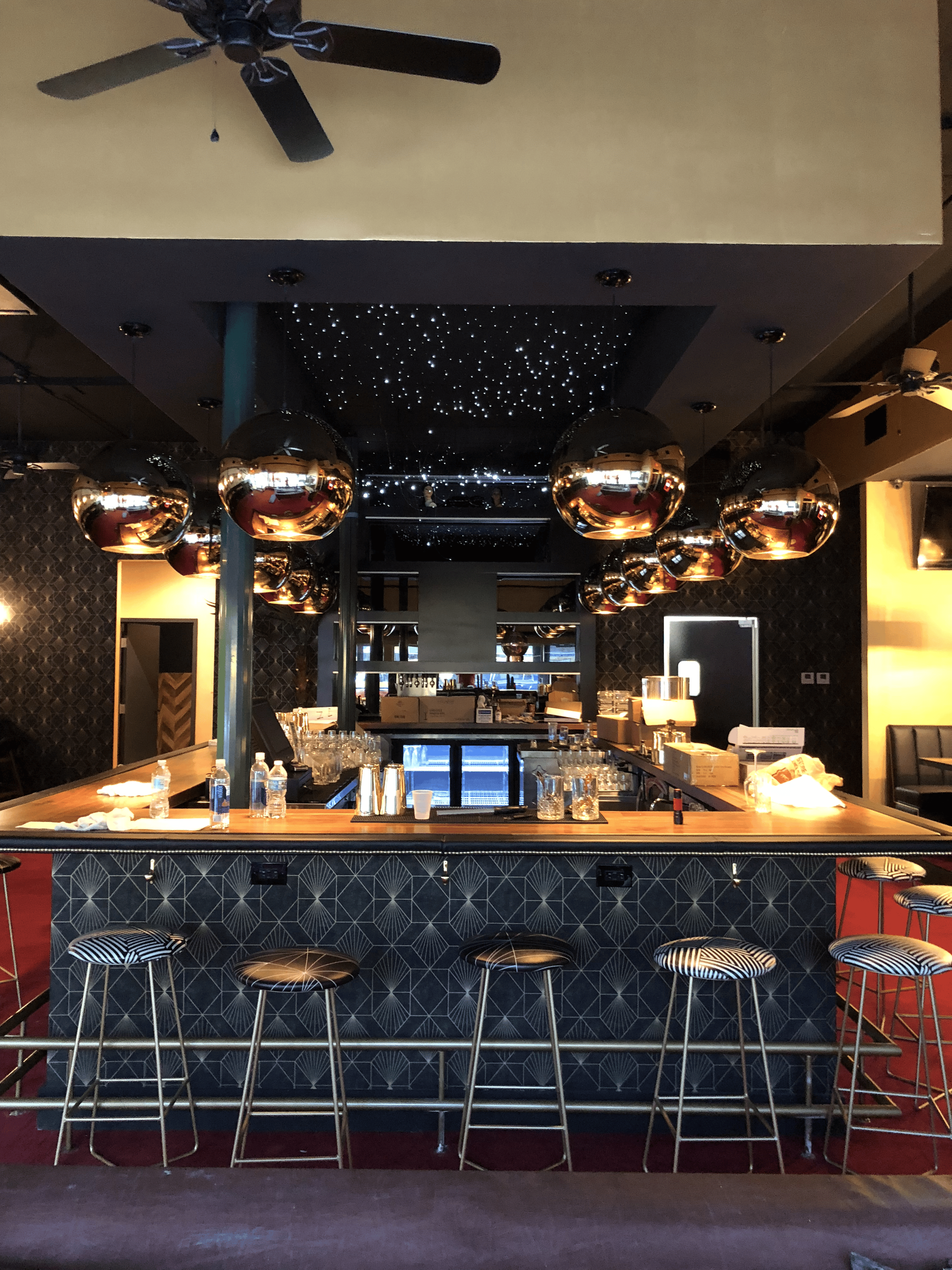 Bar interior with copper pendant lights, star-effect ceiling, and patterned bar stools.