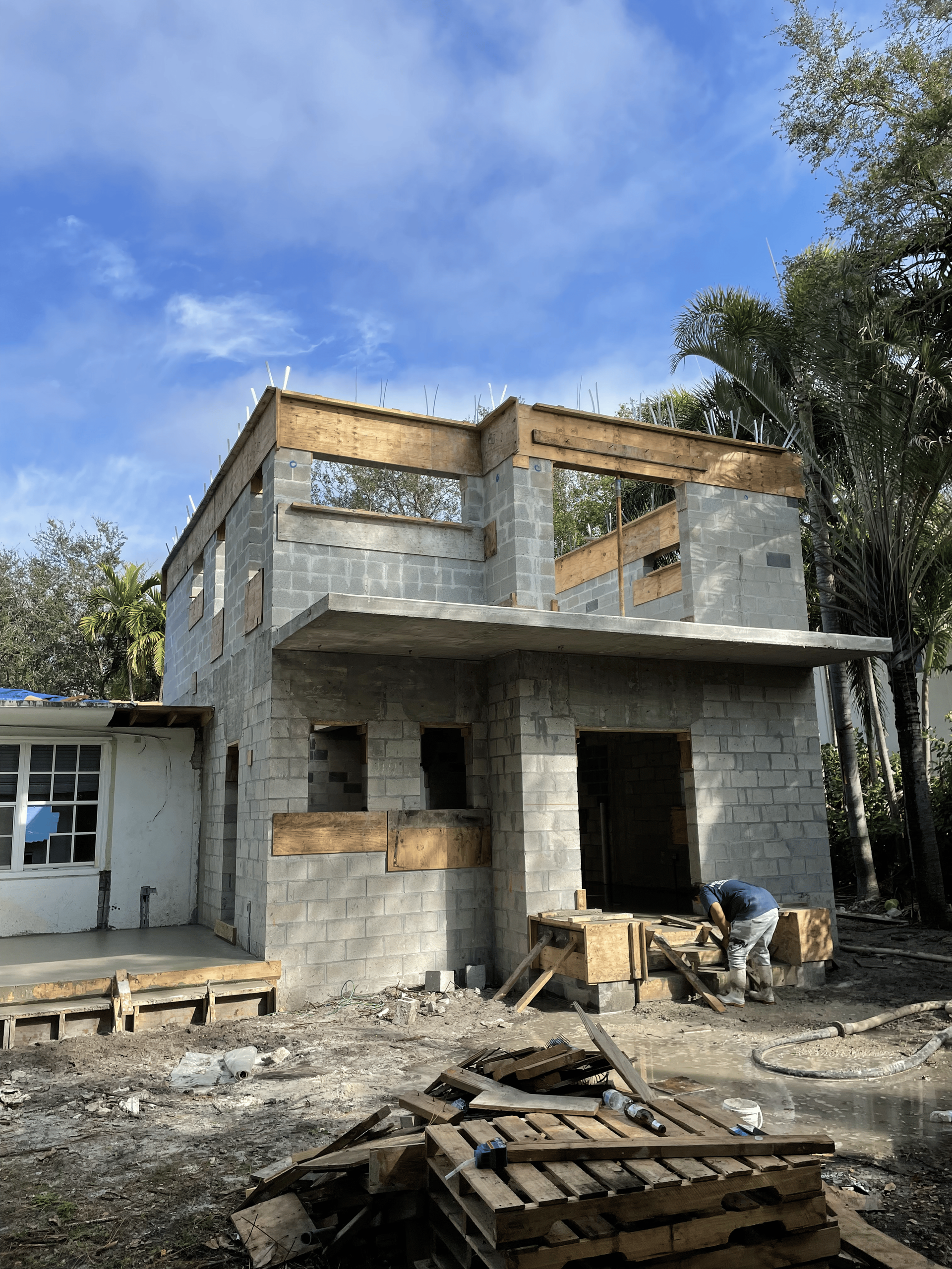 Two-story house under construction, concrete block walls.  A person works at the front entrance.  Sunny day.