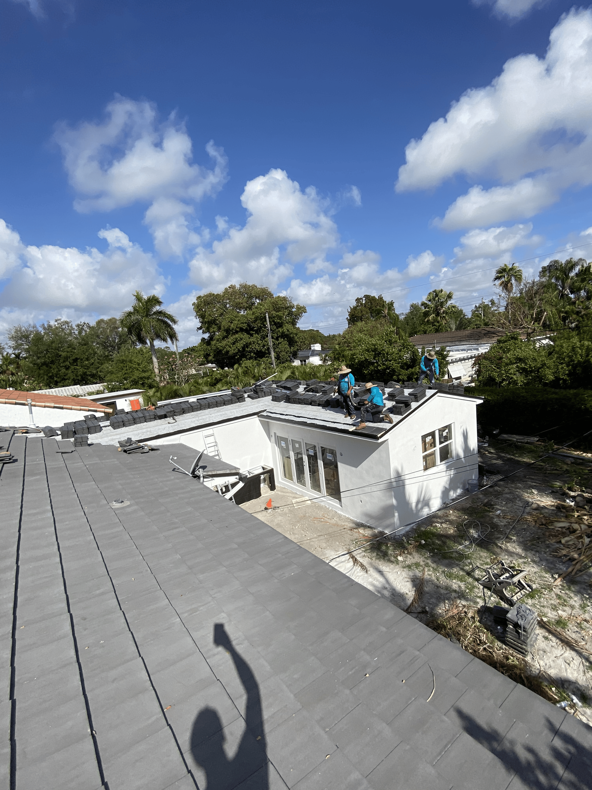 Workers installing a gray roof on a white house under a sunny sky.