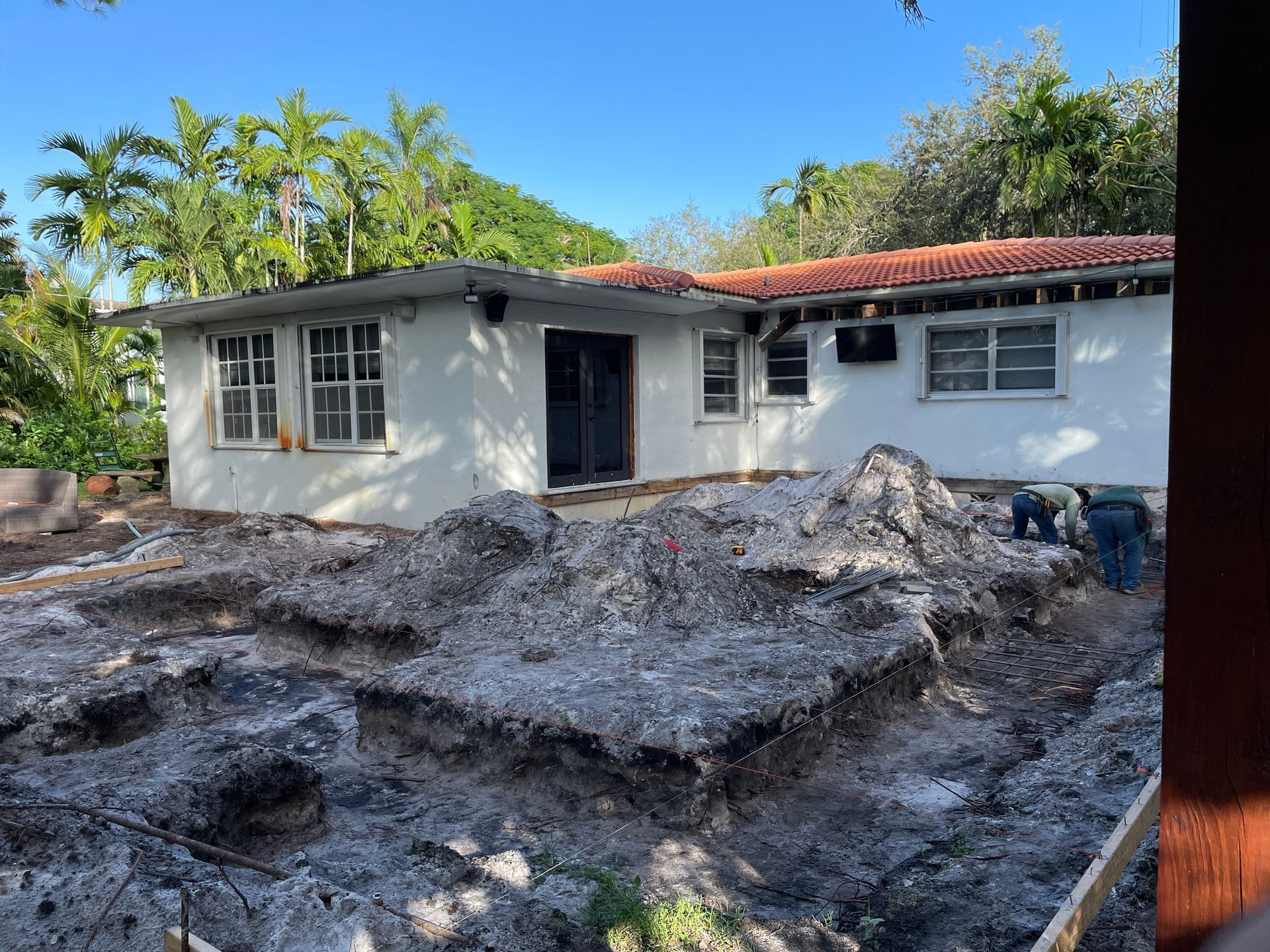 House under construction with dirt pile in front. Palm trees in background.