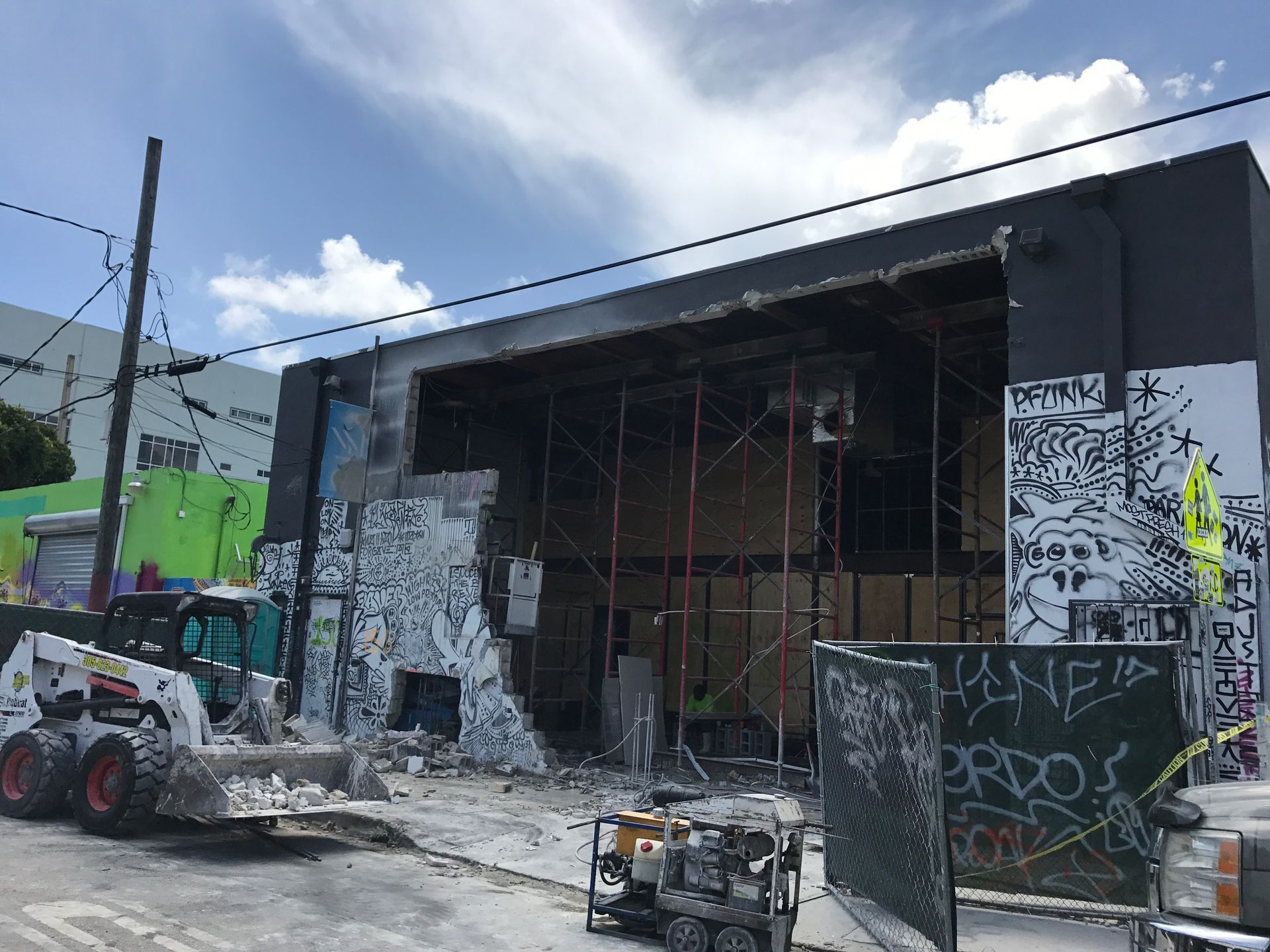 Building demolition in progress; construction equipment and scaffolding visible. Graffiti art adorns the damaged walls.