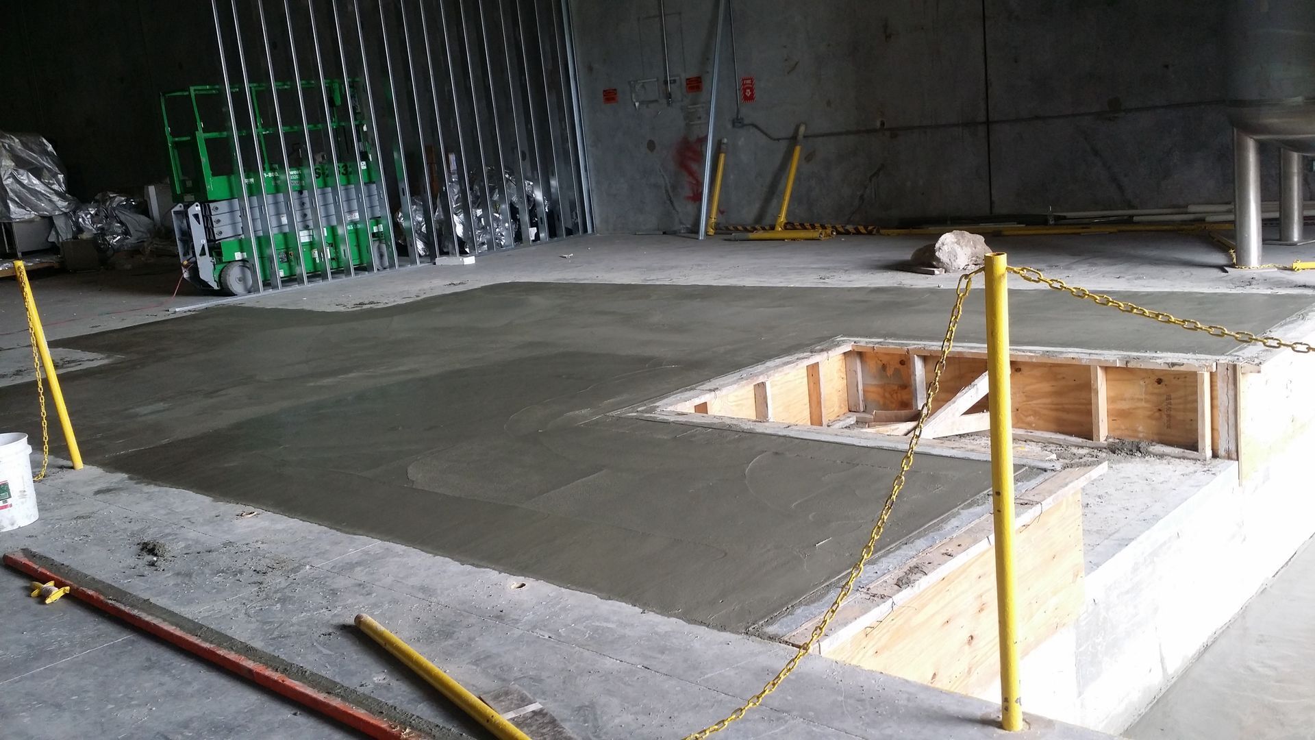 Freshly poured concrete floor in a construction site, with a recessed opening and safety barriers.