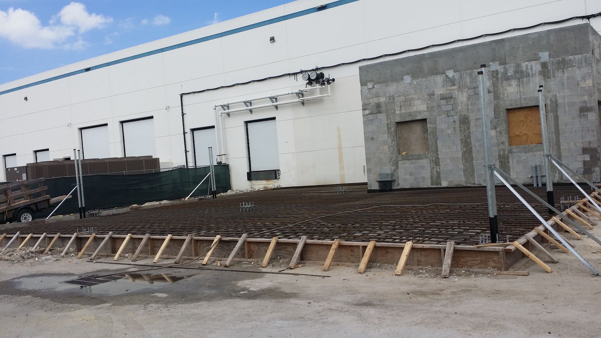 Construction site with exposed concrete foundation in front of a white industrial building.