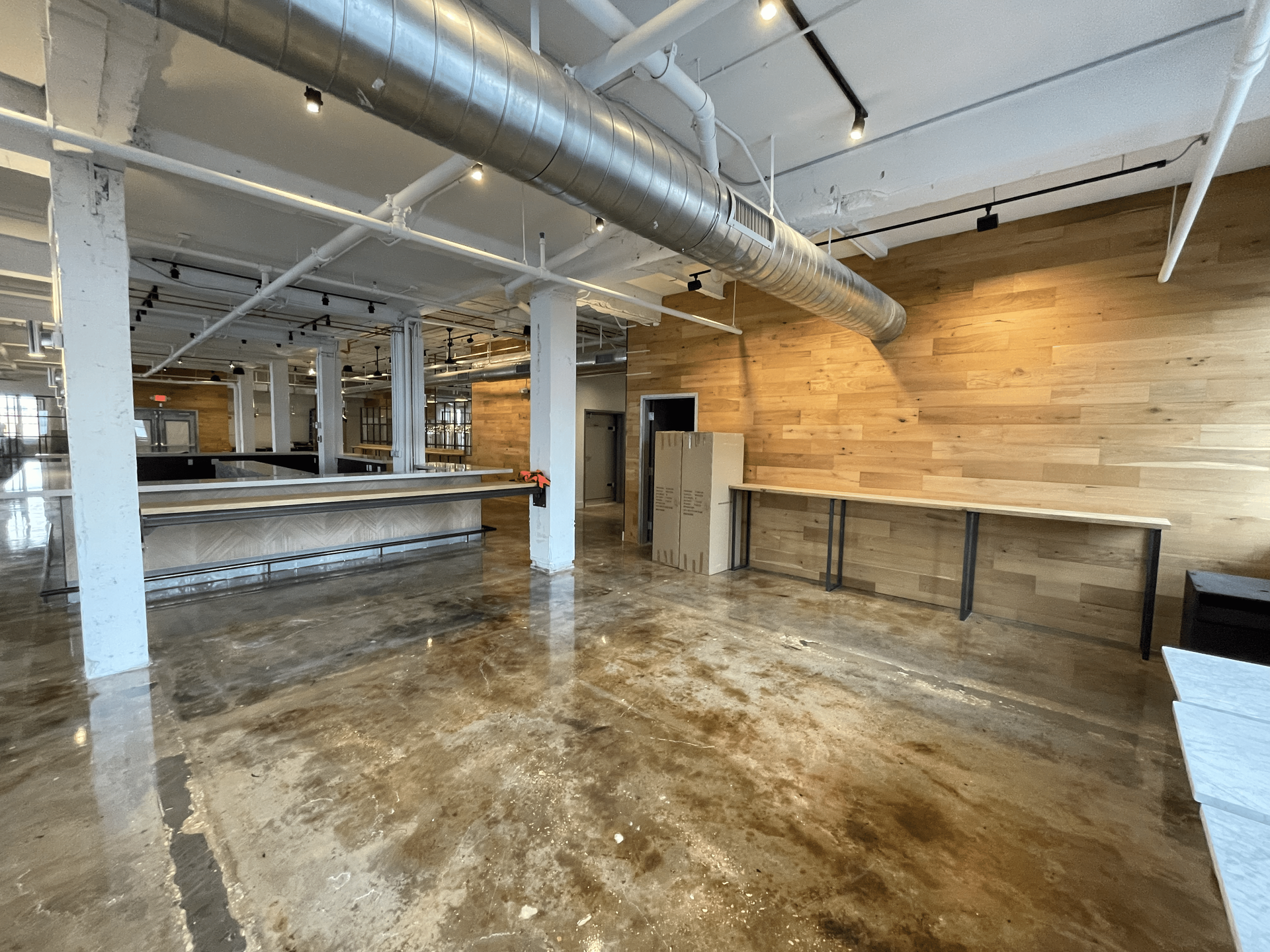 Spacious, empty commercial interior with exposed beams and concrete floor. Wooden accent wall and counters.