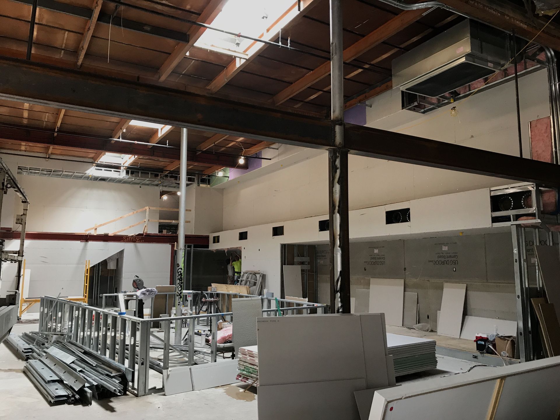 Interior construction site with exposed beams, drywall, and metal framing.