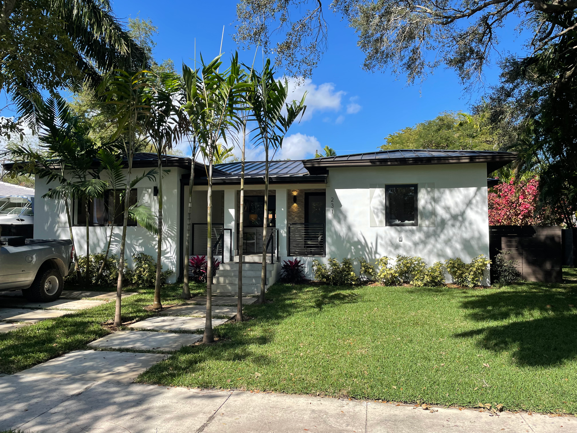 White house with a dark roof and small trees in front of a green lawn under a blue sky.