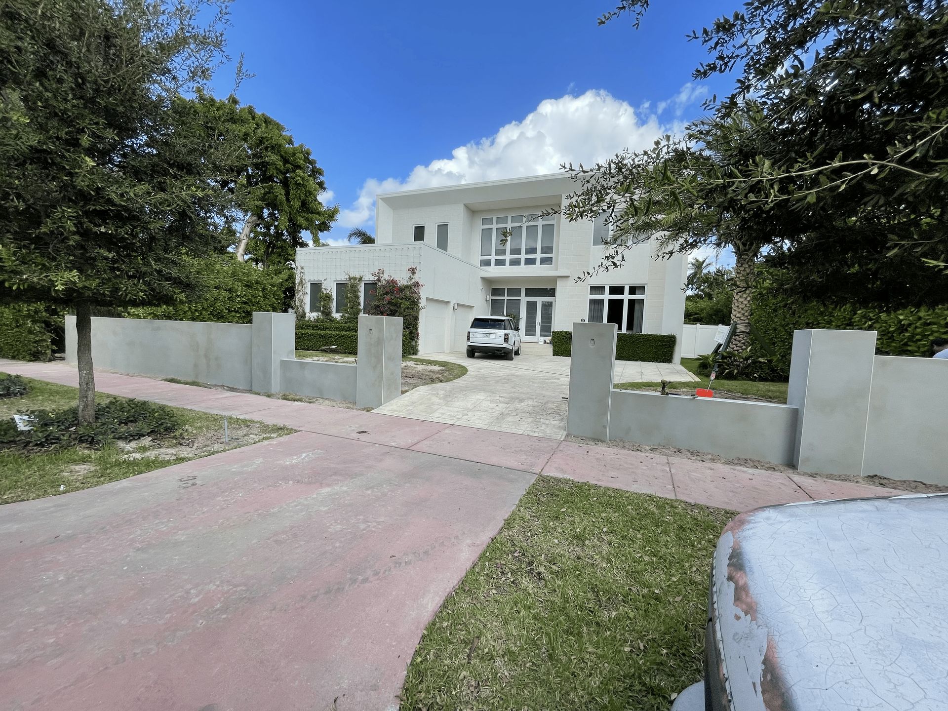 White modern house with a gray fence and a car in the driveway under a blue sky.