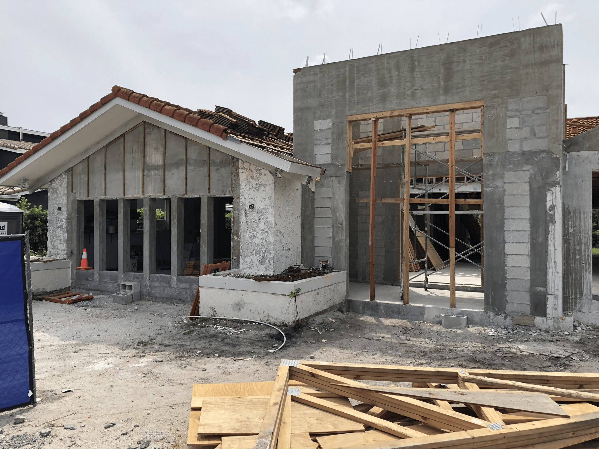 Building under construction: concrete blocks, wooden frame, visible roof tiles, and sunlight.