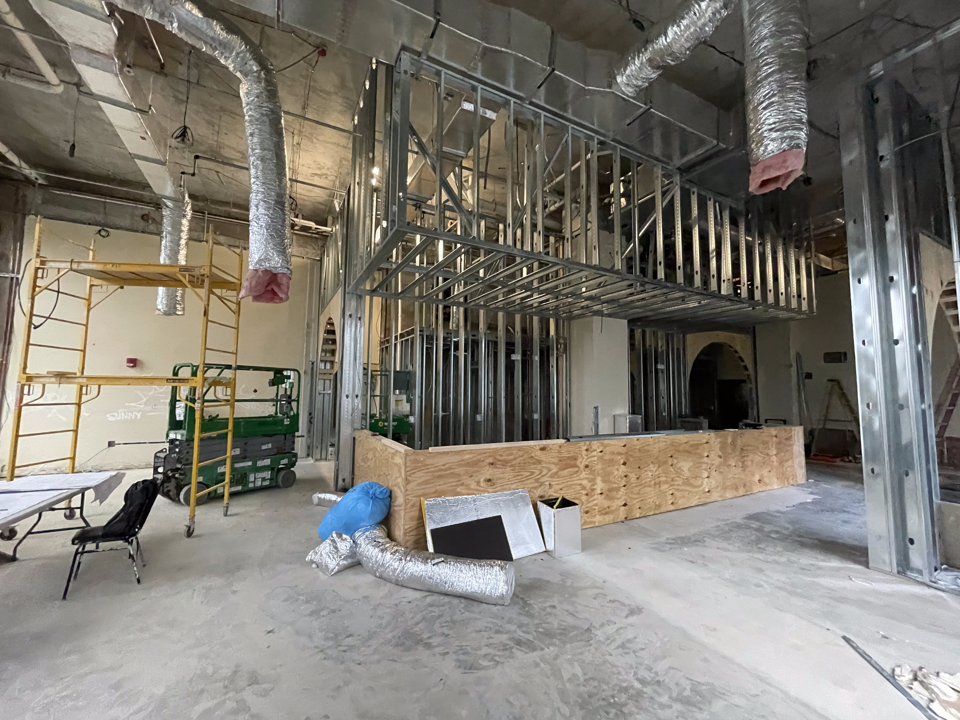 Interior construction site with metal framing, exposed ductwork, and a partial wood bar structure.