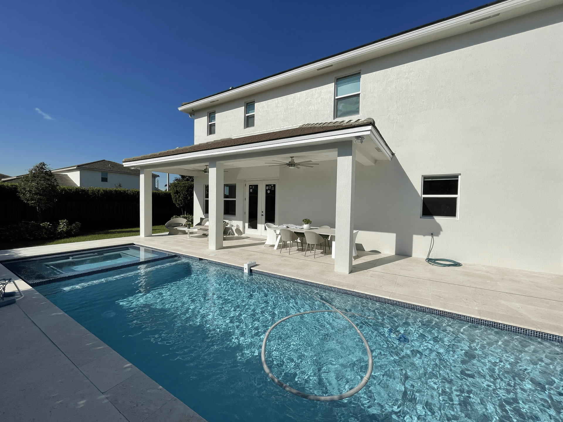 Backyard with pool, patio, and two-story white house on a sunny day.