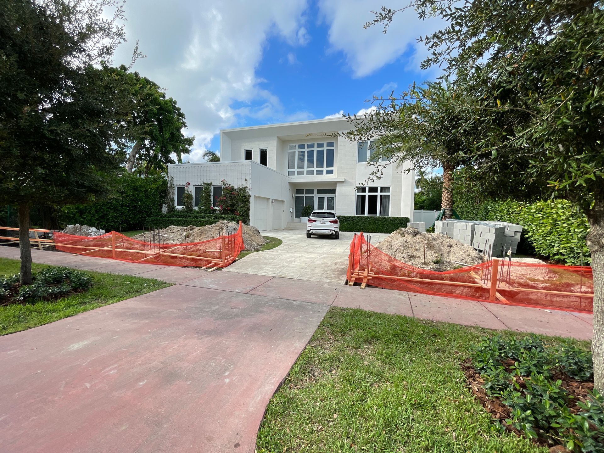 White house with a car in the driveway, under a blue sky, construction in front.