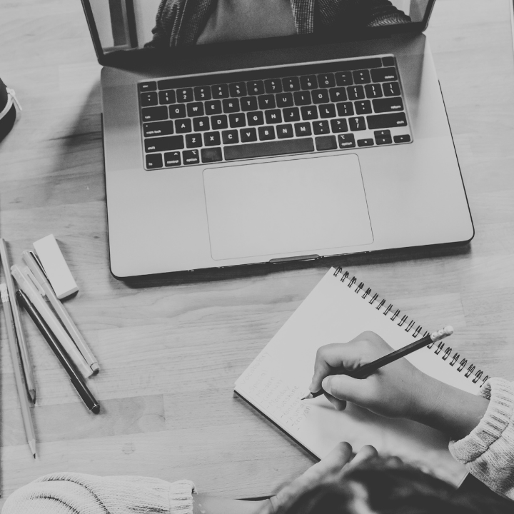 Person writing in a notebook at a desk with a laptop, pencils, and eraser.
