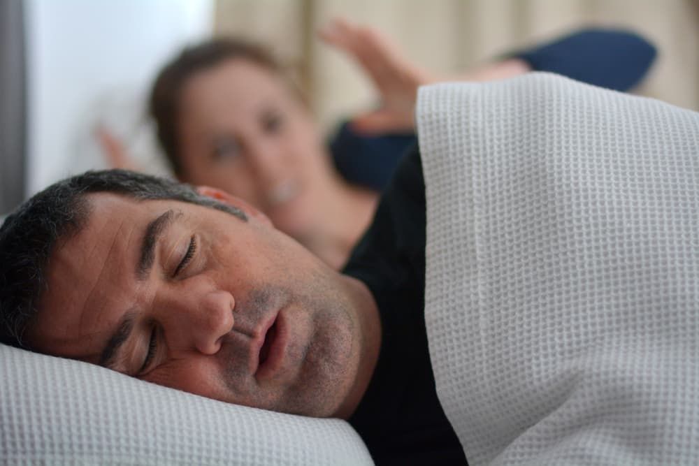 A Man is Sleeping in a Bed With a Woman Laying Next to Him — Advanced Dental Southern Highlands in Moss Vale, NSW