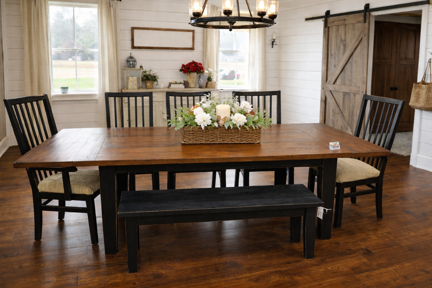 Rustic dining room with a long wooden table, black chairs, bench, chandelier, and barn-style doors.