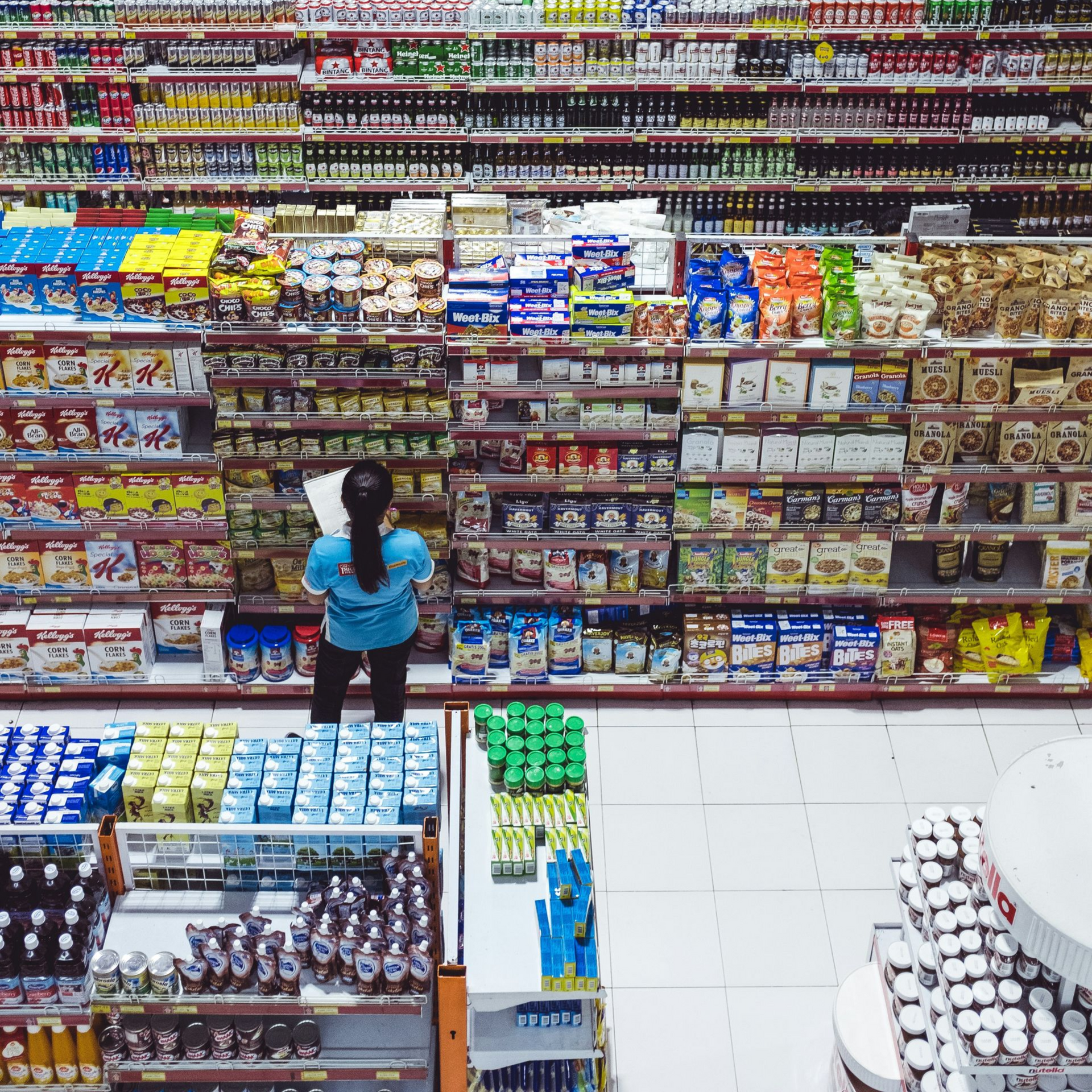 Shop manager reviewing stock on shelves. Several rows of stock extend behind the shelves.