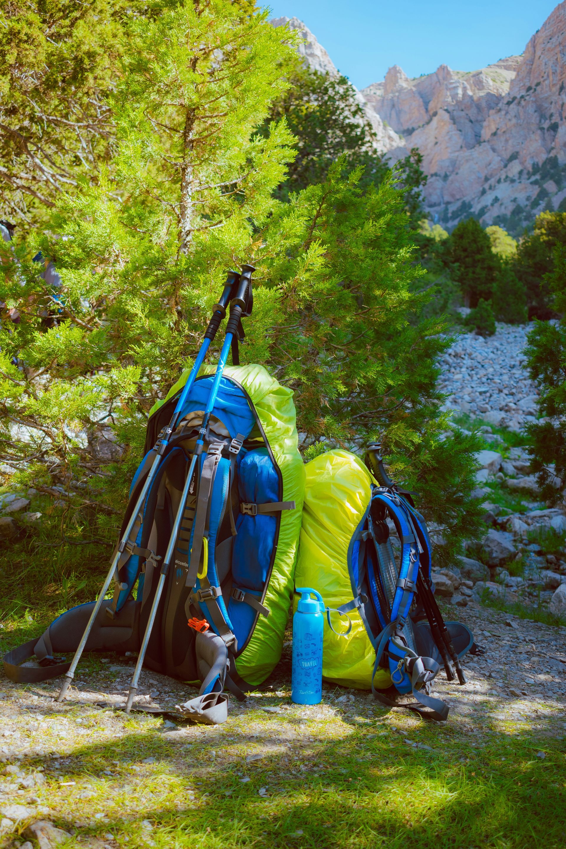 Two backpacks and a pair of walking poles in front of a stony stream bed.