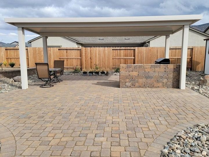 Paver patio with a white pergola, built-in brick grill, and brown fence in the background.