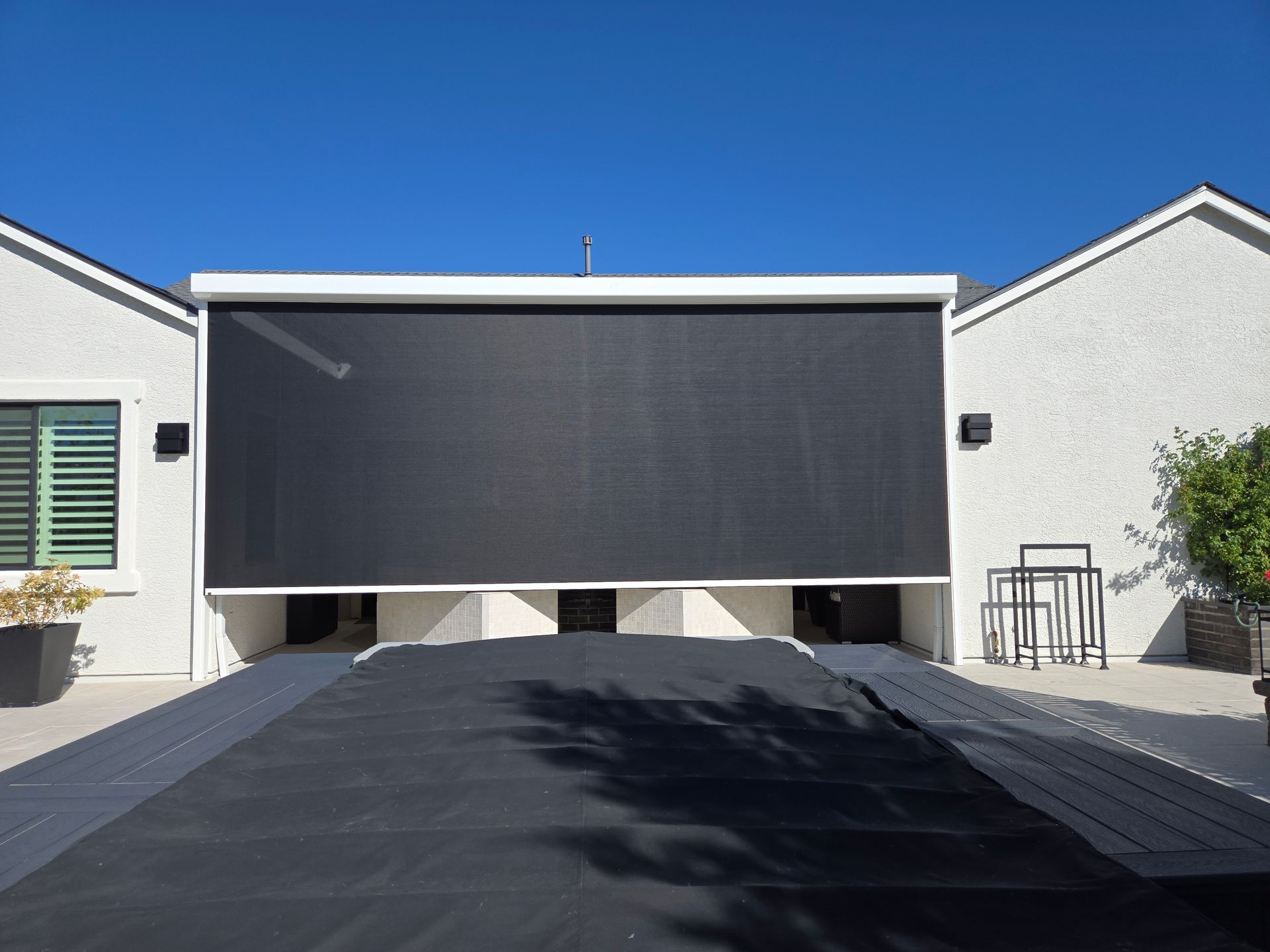 Outdoor sun screen covering pool, between two white buildings on a sunny day.
