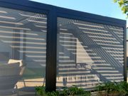 Black pergola with mesh screens, casting striped shadows on outdoor furniture.