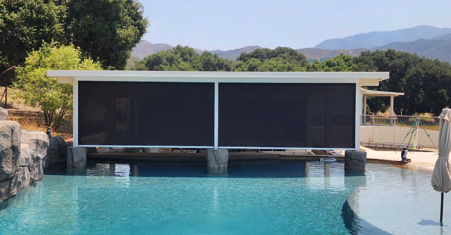 Poolside structure with dark shades over water, mountains in background.