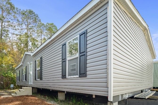 A gray modular home with white trim, black shutters, and a blue sky background.