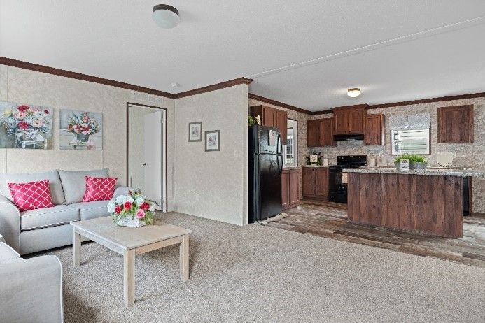 Living room and kitchen in a home. Gray couch with pink pillows, coffee table, and kitchen with wood cabinets and island.