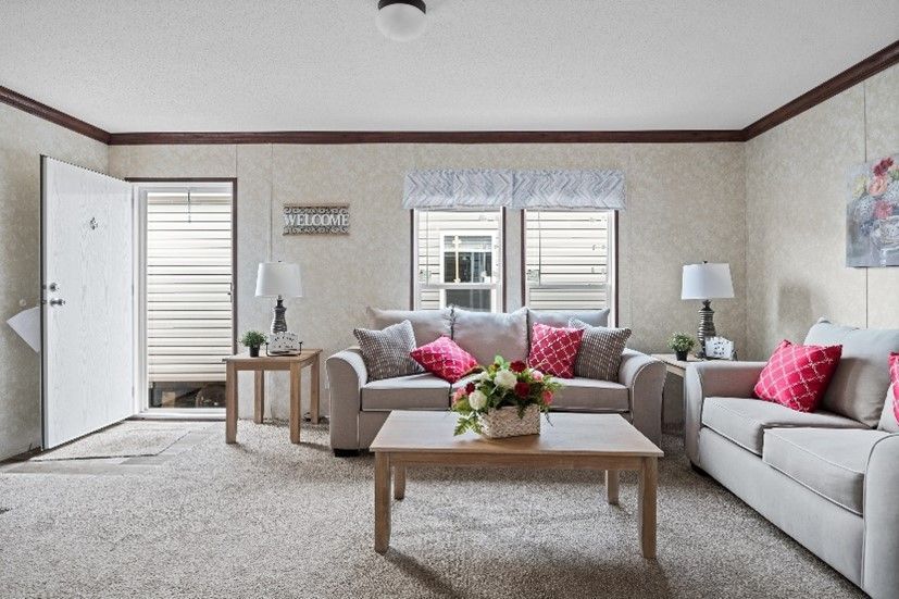 Cozy living room with beige couches, pink pillows, and a coffee table in front of windows with blinds. A door is open on the left.