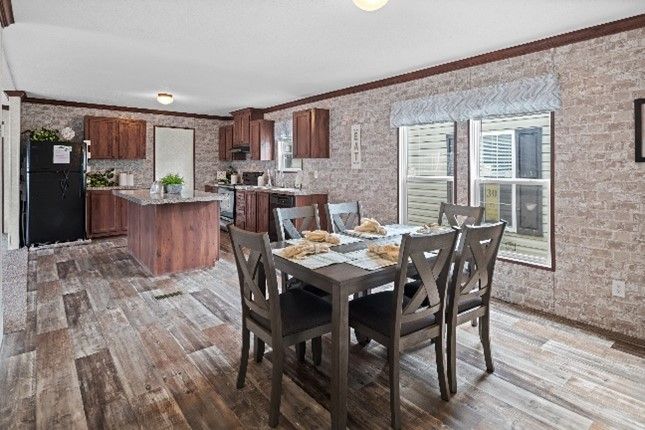 Open-plan dining room and kitchen. Wooden dining table with six chairs, and kitchen island with cabinets; brick-style wallpaper.