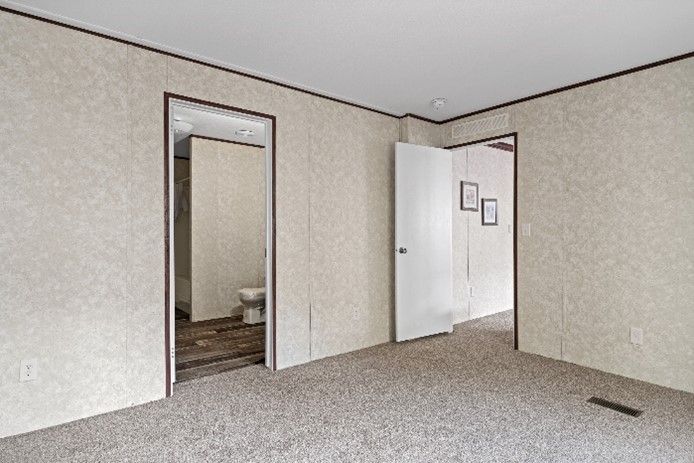 Empty room with carpet, textured walls, and three doorways leading to a bathroom and other rooms.