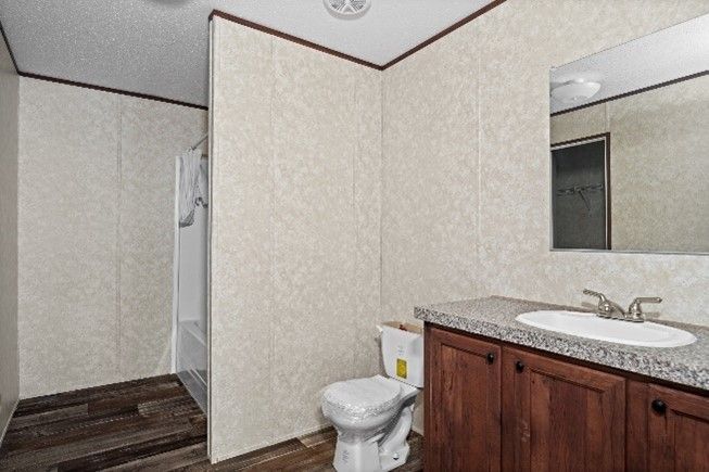 Bathroom with brown vanity, toilet, and shower with brown flooring. Beige walls and a large mirror above the sink.