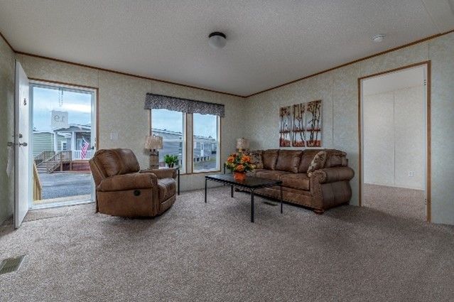 Cozy living room in a mobile home with brown furniture, beige carpet, and a view of the outside.