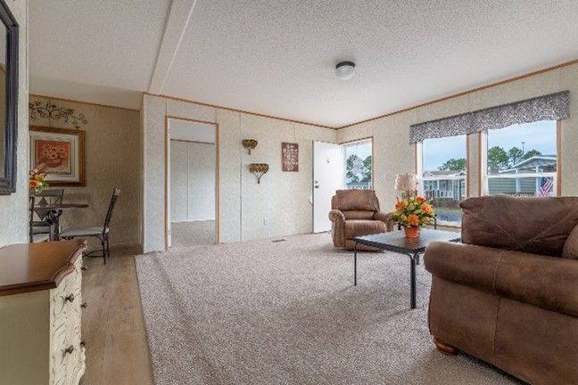 Cozy living room with brown leather furniture, a neutral carpet, and light-colored walls and trim. Natural light streams in from the windows.