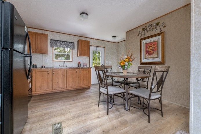 A kitchen and dining area with wooden cabinets, a black refrigerator, a round table, and a floral arrangement.