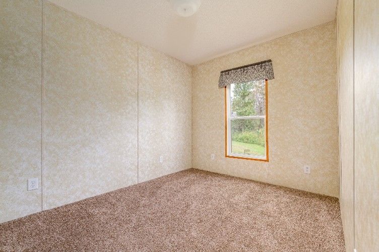 Empty room with tan walls, brown carpet, and a window with a forest view, under a patterned valance.