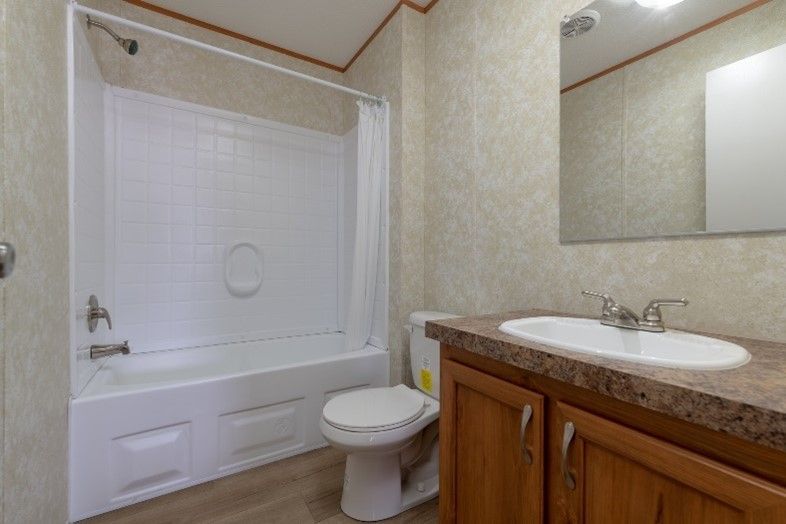 Bathroom with white tub and shower, toilet, brown vanity, and beige walls.