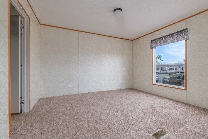 Empty bedroom with tan carpet, beige walls, a window with a valance, and a light fixture.