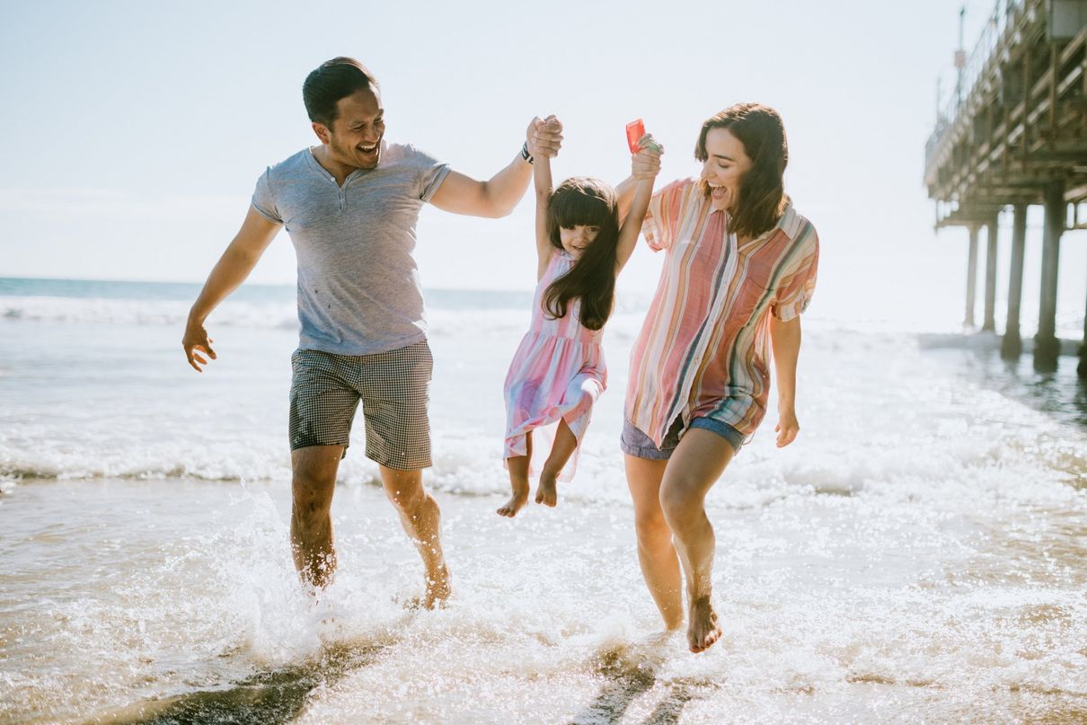 parents swinging child over ocean