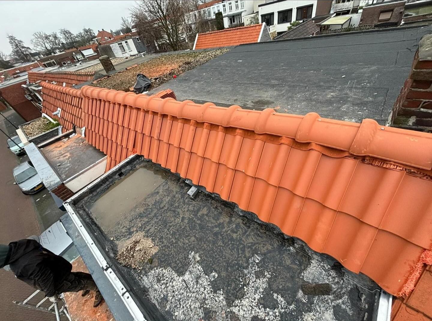 een man staat op het dak van een gebouw met rode dakpannen.