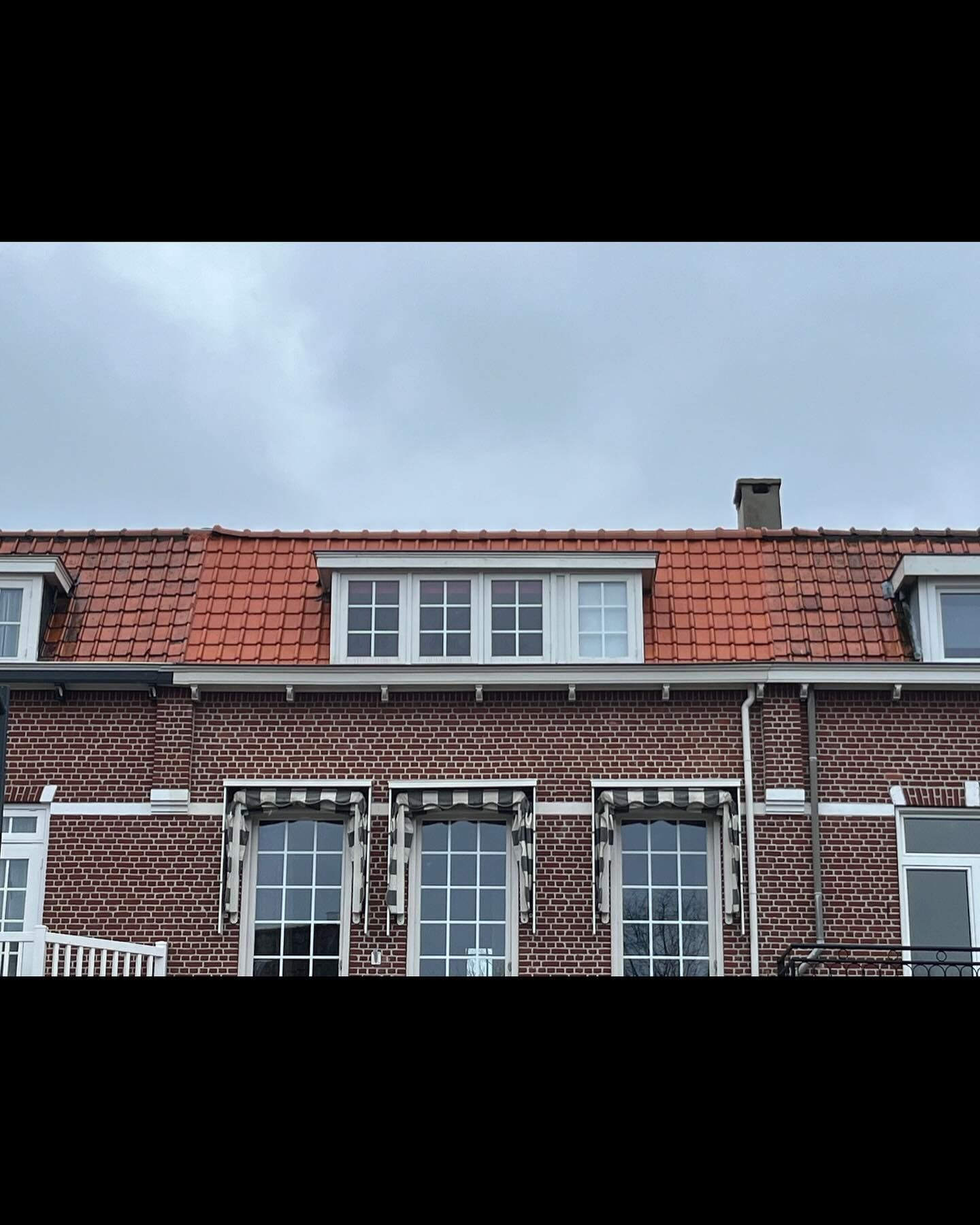 een bakstenen gebouw met een rood pannendak en witte ramen