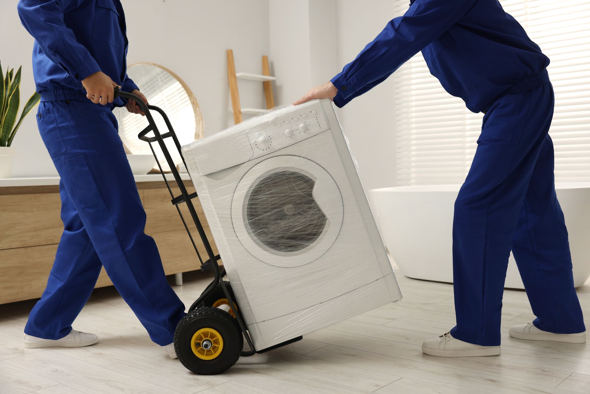 Two men are carrying a washing machine on a dolly.