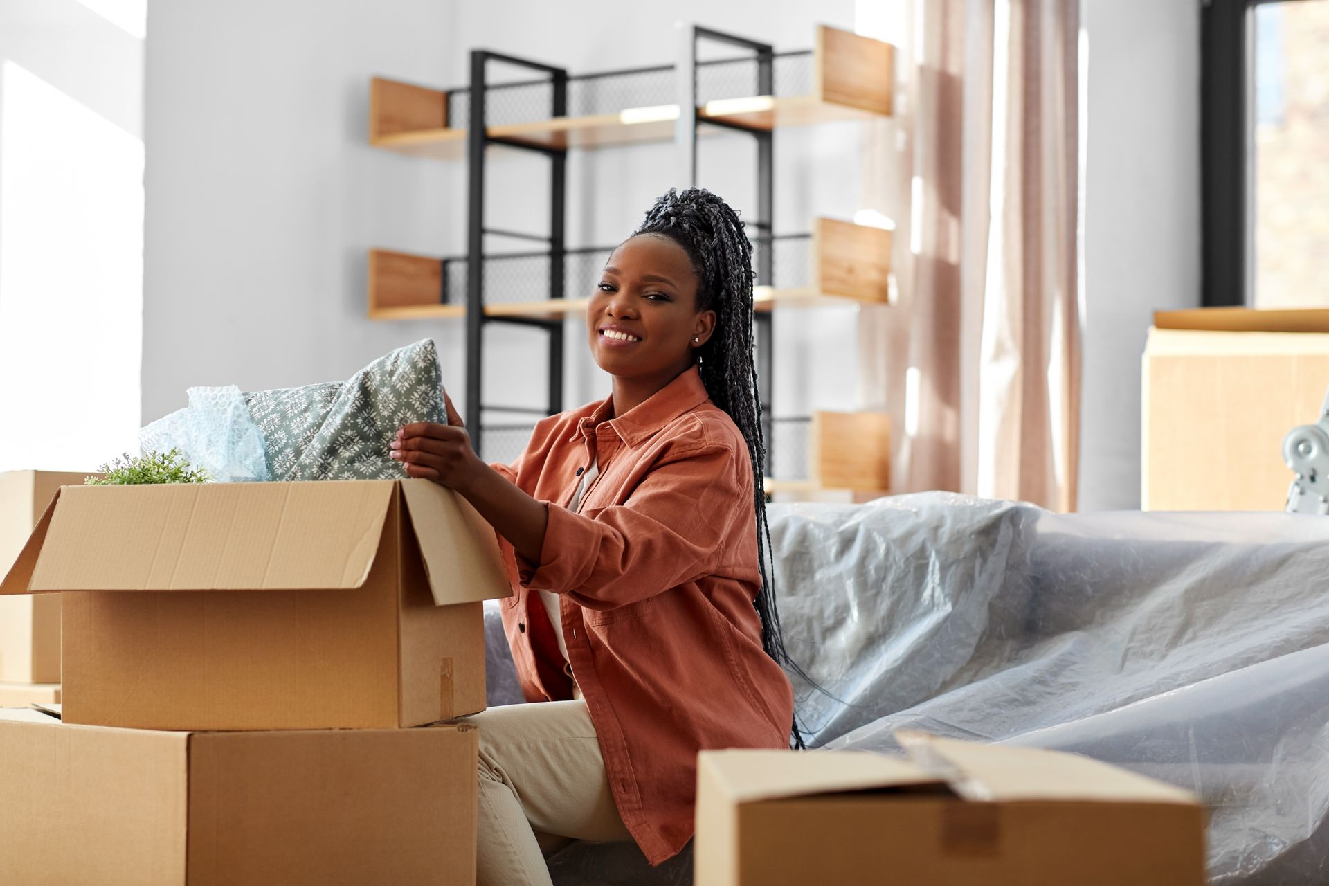 Black woman unpacking a box, smiling, in a room with moving boxes.