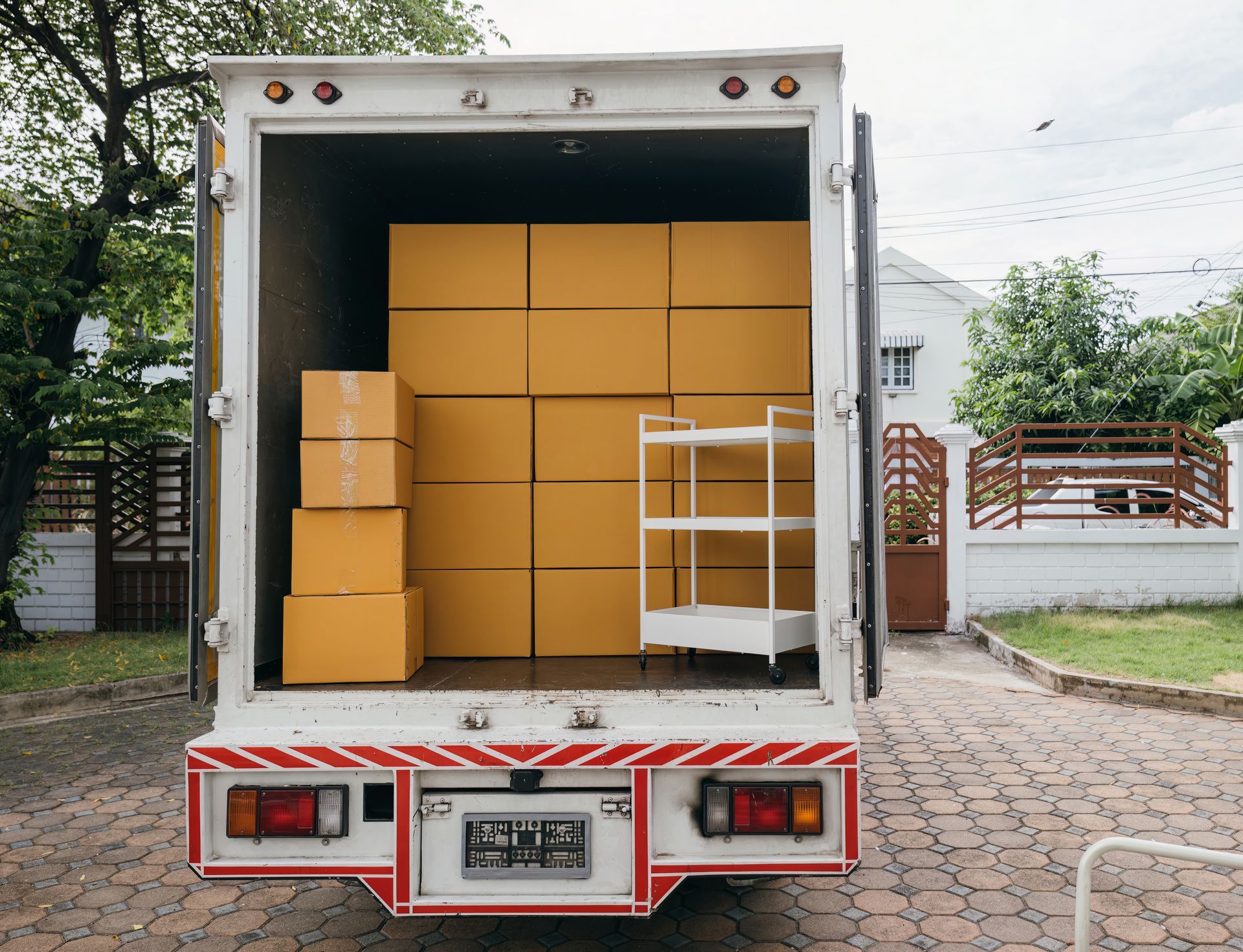 A delivery truck with boxes and a shelf inside, parked on a driveway in front of a house.