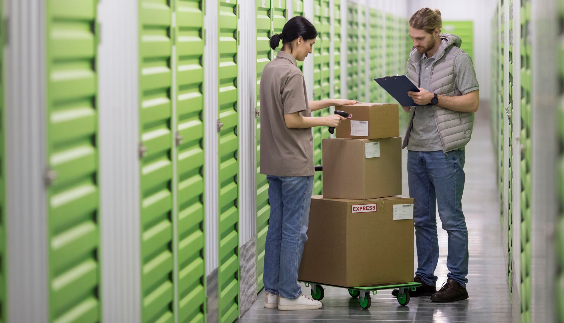 Two people, a man and woman, in storage unit hallway by boxes, checking inventory.
