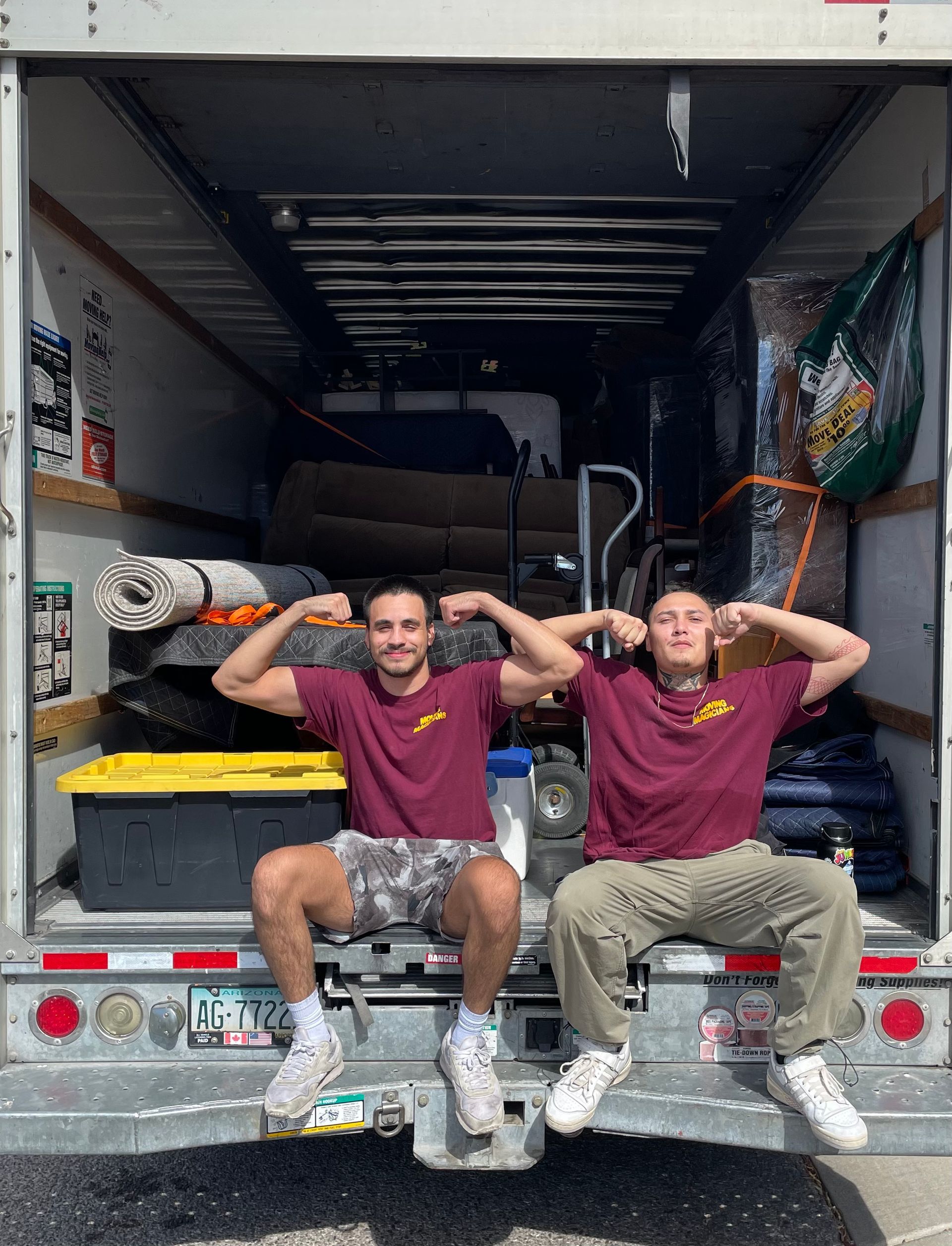 Two men are sitting on the back of a moving truck.