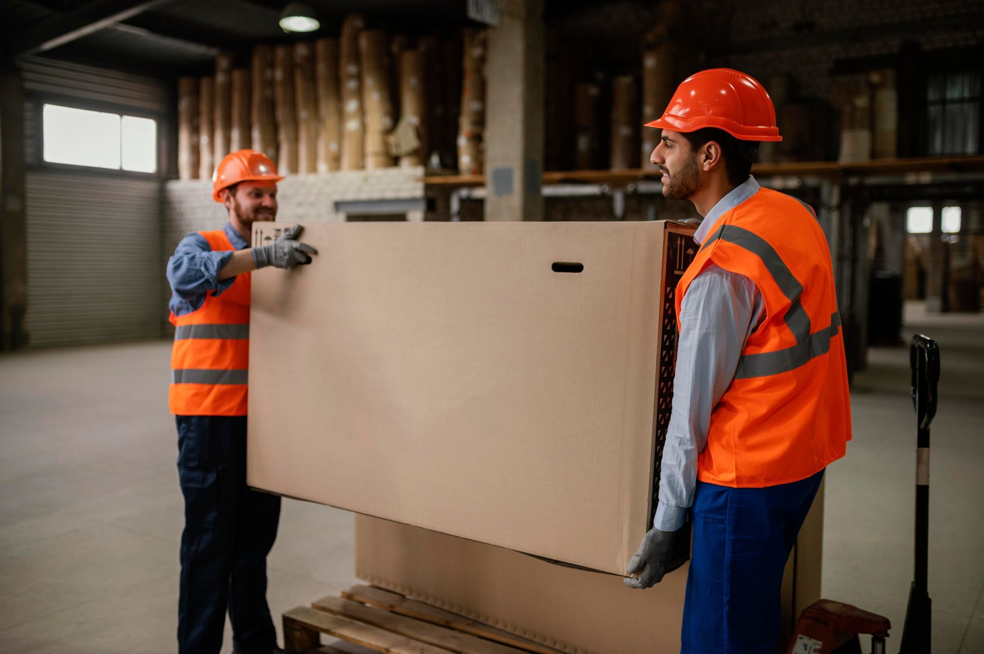 Two men are carrying a large piece of wood in a warehouse.