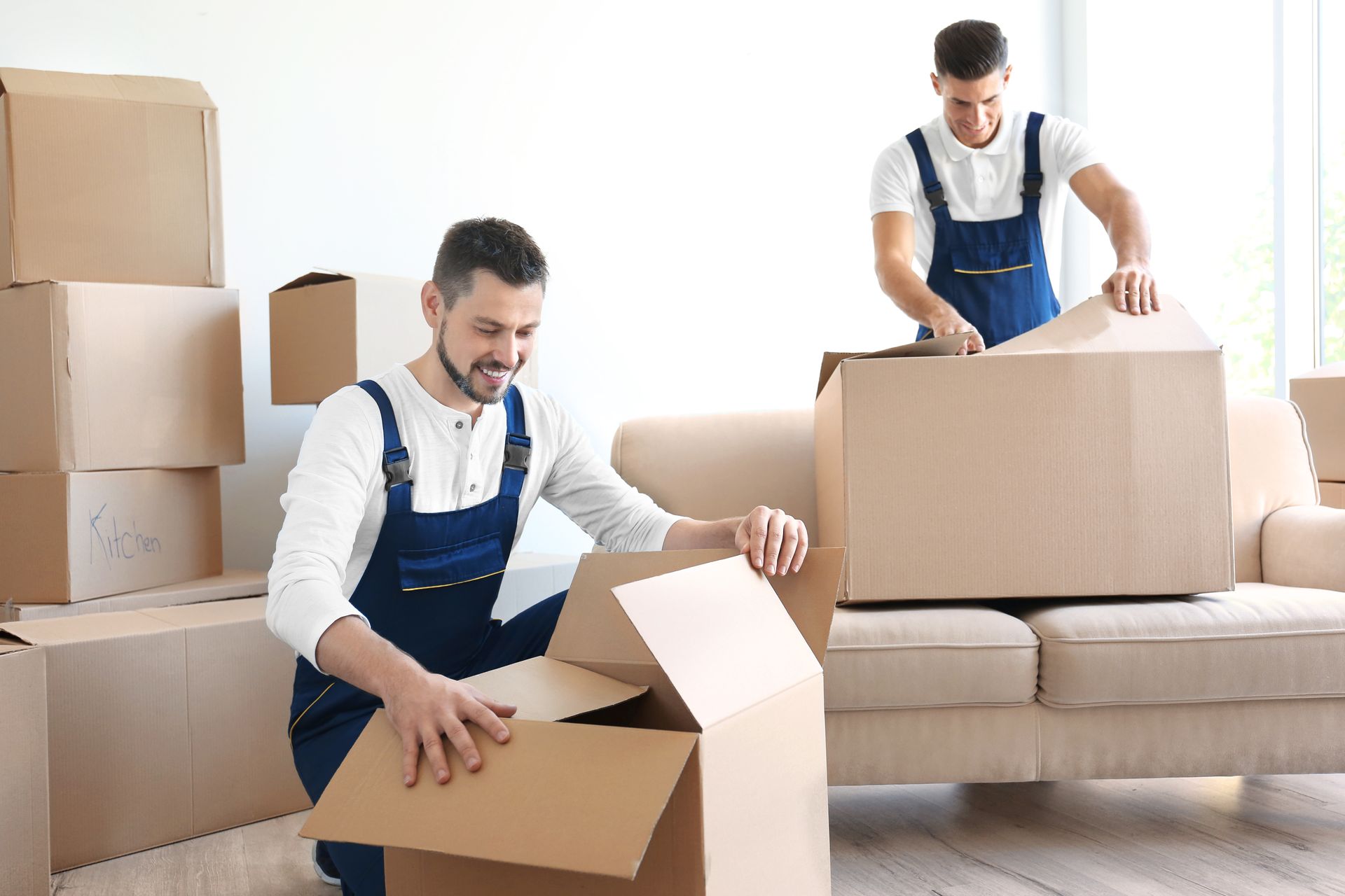 Two men are moving boxes in a living room.