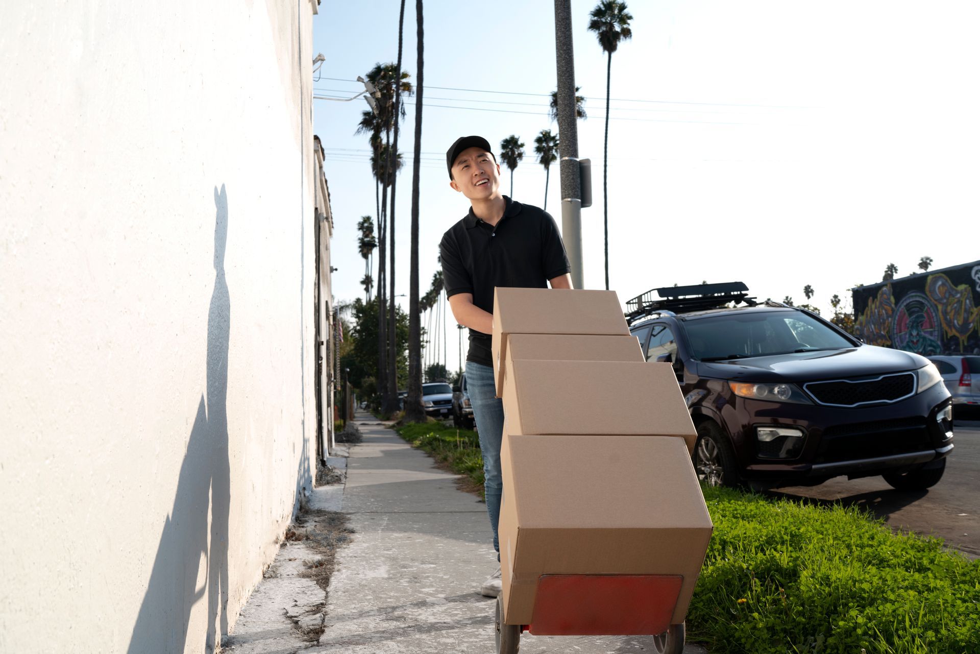 A man is pushing a cart full of boxes down a sidewalk.